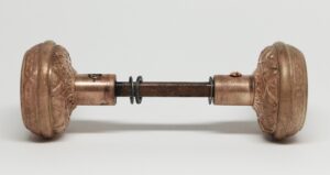 Pair of brass door knobs with an attached spindle, shown side on with ornate four-fold detailing and visible surface wear.