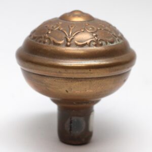 Close-up of an antique brass passage door knob with a domed, embossed top and a threaded stem.