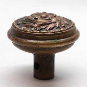 Close-up of an antique bronze door knob with a Romanesque swirl top and a visible screw hole in the stem.