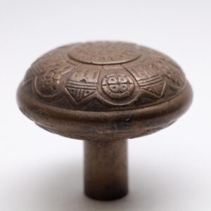 Antique bronze door knob with a domed top and embossed sixfold floral pattern.