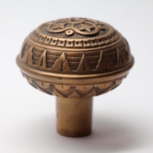 Antique bronze door knob with a domed, fourfold floral pattern and a cylindrical stem.