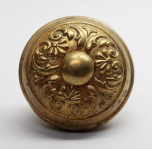 Antique brass Colonial door knob with ornate floral scroll relief and a domed center, shown in close-up.