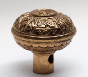 Close-up of a Vernacular door knob with an ornate domed top and worn polished bronze finish, showing the threaded stem below.
