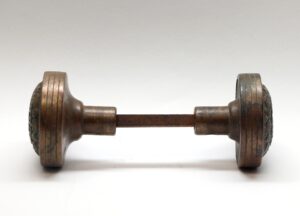 Pair of antique bronze door knobs with a spindle, shown in side view.