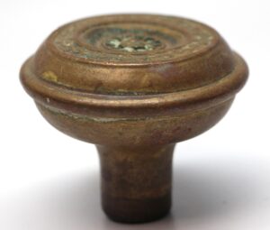 Close-up of an antique brass door knob with concentric circular detailing on the top and a short stem.