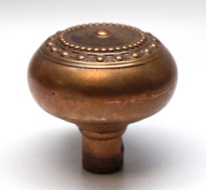 Antique brass entry door knob with a concentric beaded top and a short spindle visible below.