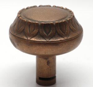 Antique bronze door knob with a radial top and sunflower leaf trim, shown in close-up.