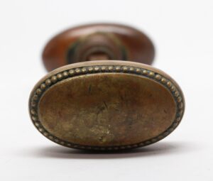 Pair of antique brass oval door knobs with beaded edges, shown in close-up from the end.