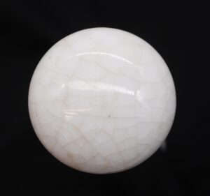 White crackled ceramic door knob shown in close-up against a dark background.