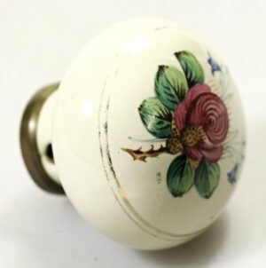 Hand-painted porcelain door knob with a pink flower and green leaves on a white knob, shown in close-up with surface wear visible.