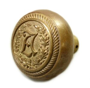 Antique bronze passage door knob with an ornate circular emblem and centered lettering, shown as a single knob in close-up.
