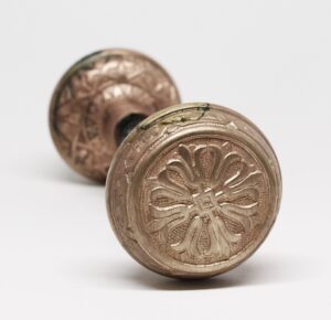 Pair of brass door knobs with fourfold floral rosettes, shown in close-up with one knob in front and the other slightly behind.