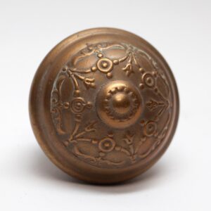 Antique brass door knob with ornate Victorian floral relief and a round, domed center.