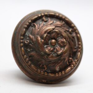 Antique bronze door knob with a Romanesque swirl pattern and beaded border, shown in close-up.