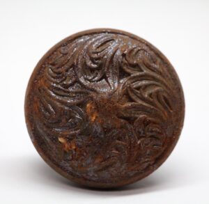 Close-up of a cast iron door knob with a carved swirl pattern and visible surface wear.