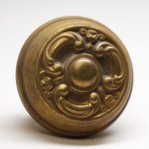 Antique brass French door knob with an ornate three-fold rosette and domed center, shown in close-up.