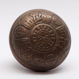 Antique bronze door knob with a six-fold patterned face and worn surface detail.