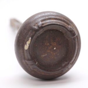 Close-up of a cast iron door knob with a dark black patina and surface wear, showing the rounded face and four-fold detailing.