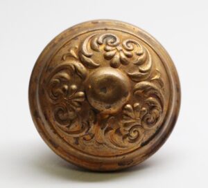 Antique brass Colonial door knob with an ornate floral relief and worn surface, shown in close-up front view.
