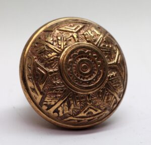 Polished bronze door knob with a raised circular center and engraved geometric pattern.