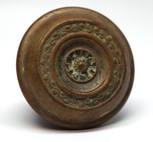 Antique brass passage door knob with concentric rings and a floral center detail.