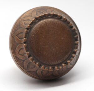 A vintage bronze door knob with a radial face and sunflower leaf trim is shown in close-up from the front.