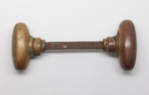 Pair of antique brass oval door knobs with beaded edges and a connecting spindle, shown side by side.