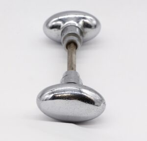 Pair of oval chrome-plated door knobs with a spindle, shown in a front view.