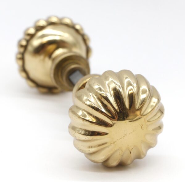 Pair of fluted brass door knobs with a polished finish, shown as a close-up of one knob and part of the spindle.