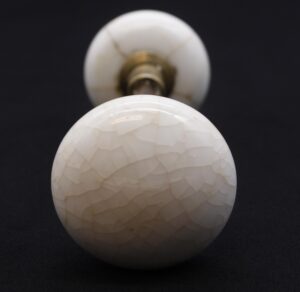 Pair of white crackled ceramic door knobs with one knob in front and the other attached to a spindle behind it.