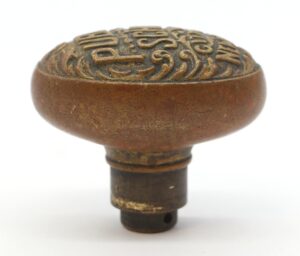 Antique bronze oval door knob with raised lettering on the top and a threaded stem below.