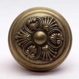 Antique brass entry door knob with an ornate Greek-style floral relief and worn surface.