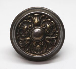 Ornate round door knob with a three-fold floral relief and dark finish.