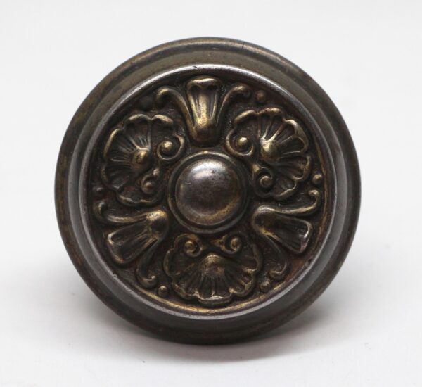 Ornate round door knob with a three-fold floral relief and dark finish.