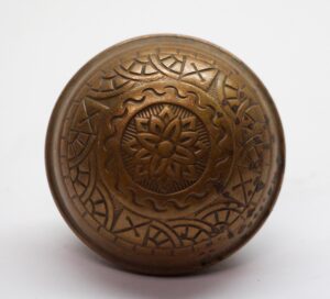 Antique brass door knob with a circular embossed floral and geometric pattern, shown from the front.