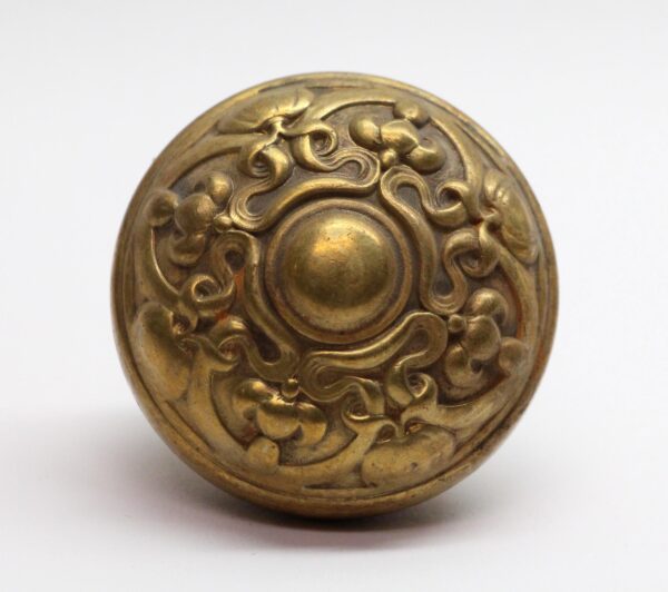 Art Nouveau brass entry door knob with ornate pressed floral scrollwork and a domed center.