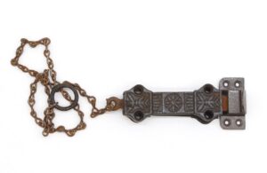 Victorian cast iron surface door bolt with chain and decorative latch plates, shown with surface mounting holes and the attached chain looped beside it.