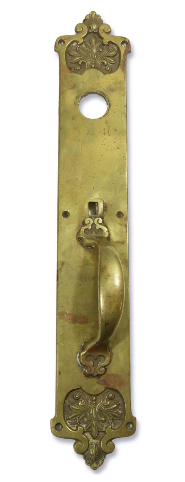 Romanesque brass door pull with an ornate backplate, a round lock hole, and a curved handle, shown front on.
