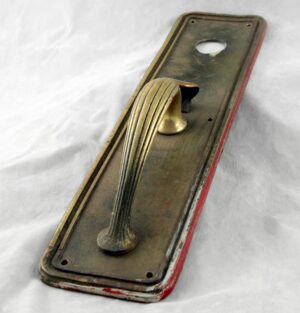 Art Deco bronze commercial door pull with a thumb latch and lock insert, shown at an angle with the Yale plate visible.