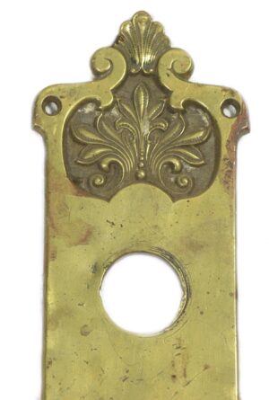 Romanesque brass door pull with an ornate top plate, a lock hole, and a large circular opening below, shown in close-up with the thumb latch missing.