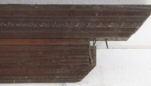 Reclaimed mahogany door header with egg and dart carving, shown in a close-up of the molded top edge and underside bracket detail.