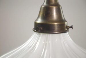 Close-up of a pendant light with an antique brass chain fitter and white fluted milk glass shade.