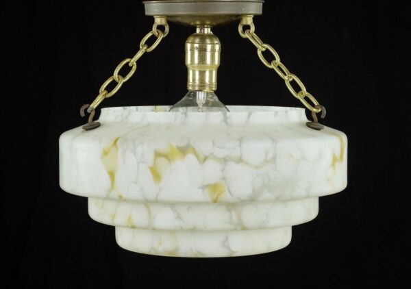 Pendant light with a white and yellow marbleized glass dish, brass chain supports, and a visible bulb socket hanging from a ceiling canopy.