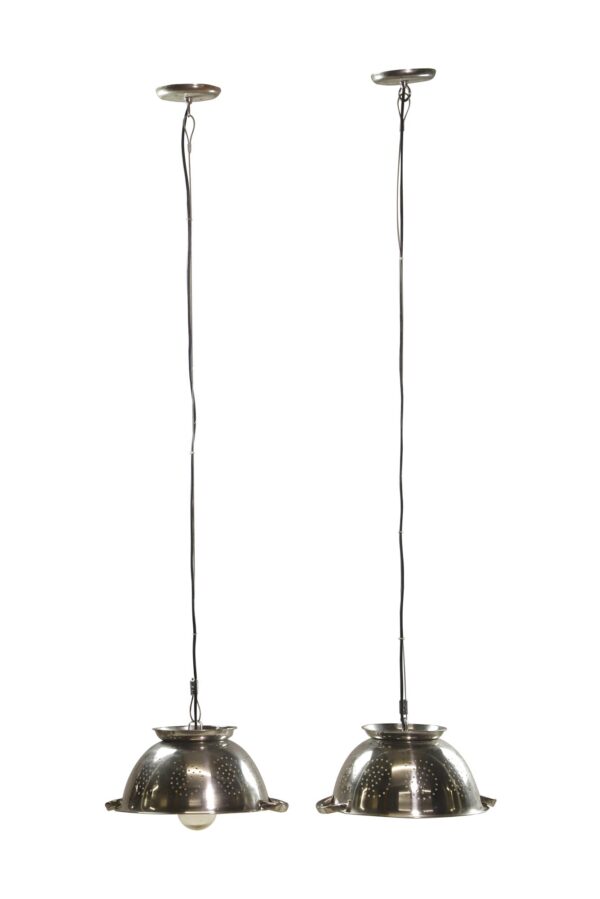 Pair of pendant lights made from colanders, each with a long cord and domed steel shade.