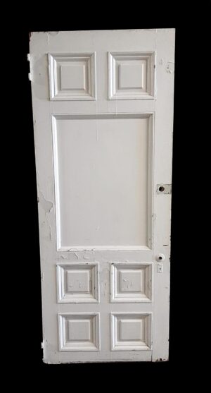 Antique wood entry door with seven raised panels, shown in white and slightly worn with visible edge damage and peeling paint.