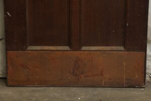 Dark wood door with four panels and lower metal protection plate, shown without glass installed in the upper openings.