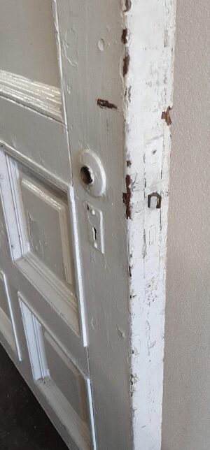 Close-up of a white wood entry door showing the edge, lock bore, and worn paint with exposed wood.