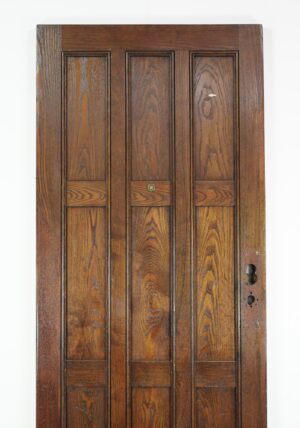 Arts and Crafts oak entry door with nine panels and a dark wood tone, shown frontally with worn hardware openings on the right edge.