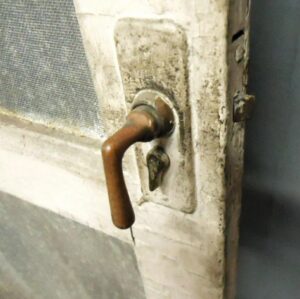 Close-up of a wood screen door showing the metal handle and lock hardware on one panel with screen above it.