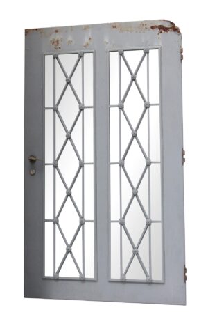 Gray steel entry door with two tall glass panels, diamond lattice design, and floral rosettes, shown with visible rust along the top edge and hardware on the left side.
